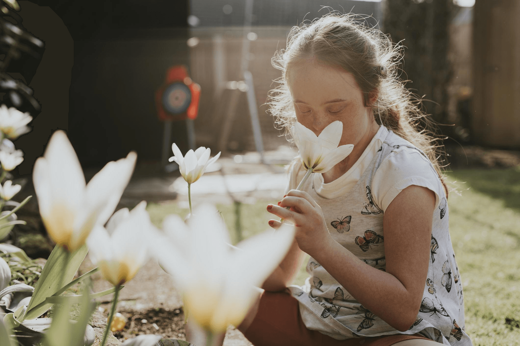 A young girl smelling white tulips in a sunlit garden